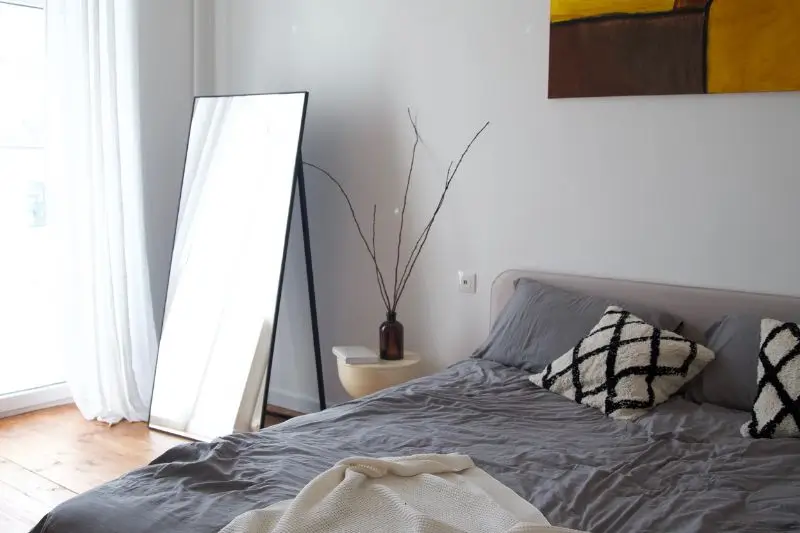 arched floor mirror reflecting window in small couples bedroom